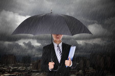 Businessman under heavy rain with storm cloud and city backgroundの写真素材