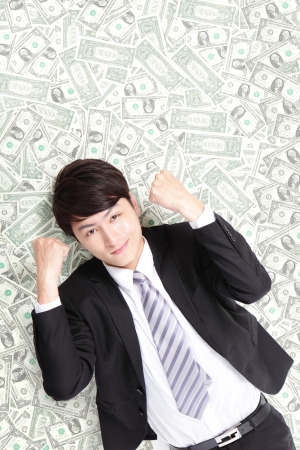 happy businessman smiling make a fist and lying on heap of money bed, asian maleの写真素材