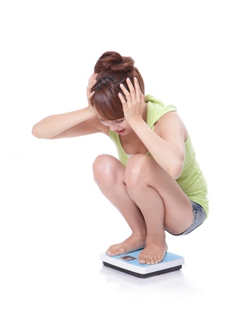 afraid young woman looking her weight on a scale isolated over white background, full length, asian modelの写真素材