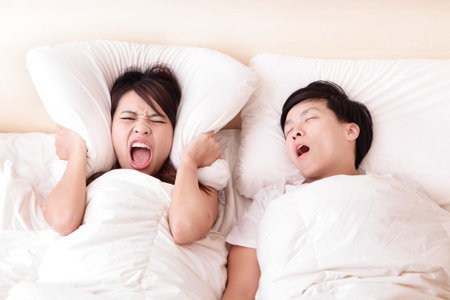 Young woman disturbed by the snores of her husband in the bedroom at home, asian familyの写真素材