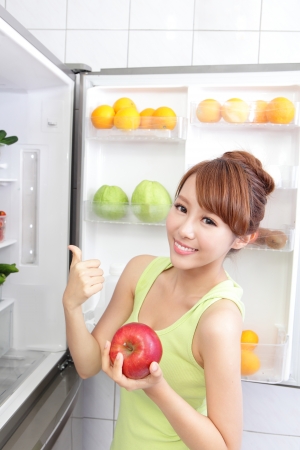 Healthy Eating Concept .Diet. Beautiful Young Woman hold apple near the Refrigerator with healthy food. Fruits and Vegetables, asian modelの写真素材