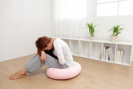 Portrait of woman with stomach ache sitting on floor at home, asian modelの写真素材