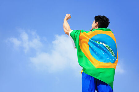 Excited man holding a brazil flag with blue skyの写真素材