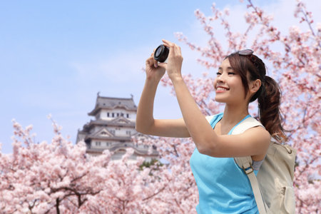Happy woman traveler take photos by camera with cherry blossoms tree and castle on vacation while springのeditorial素材