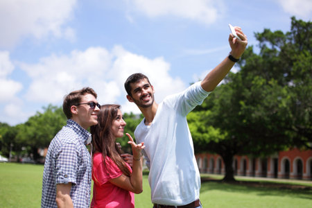 Group of happy friends taking a selfie on a blue sky in campus lawn, caucasian