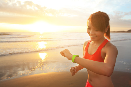 Health sport young woman run and look wear smart watch device with touchscreen on the beach at sunrise, asianの写真素材