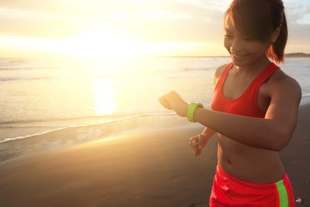Health sport young woman run and look wear smart watch device with touchscreen on the beach at sunrise, asianの写真素材