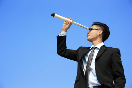 Businessman with telescope ( spyglass ) looking forward Prospects for future business with blue sky background, asianの写真素材