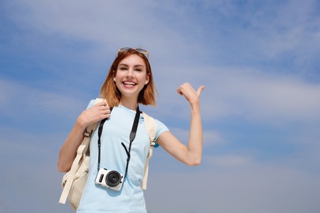 Happy travel woman smile to you and show something by finger with sky background, caucasian beautyの写真素材