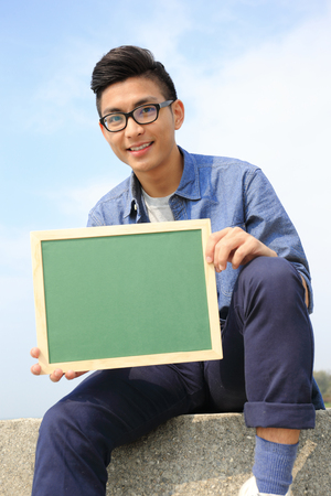 Happy man holding blackboard or chalkboardwith sky background, asian maleの写真素材