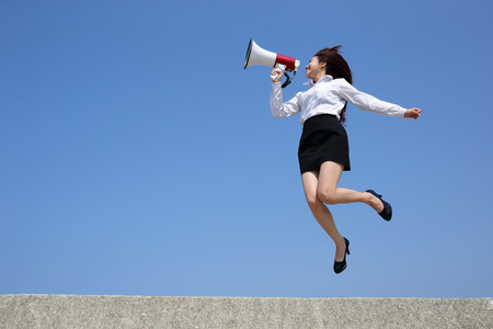 Successful business woman shouting in megaphone with blue sky backgroundの写真素材