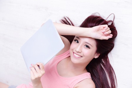 Happy young beautiful woman relax lying and using digital tablet pc, asian beautyの写真素材