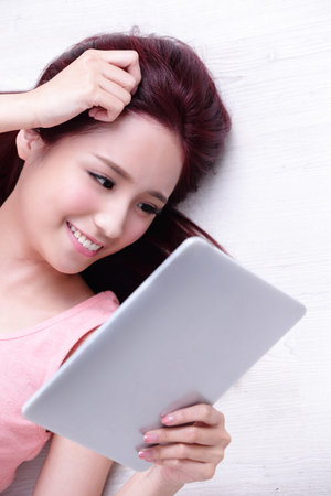 Happy young beautiful woman relax lying and using digital tablet pc, asian beautyの写真素材