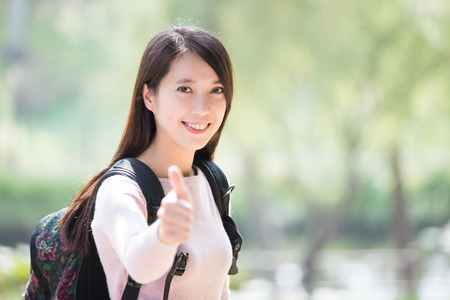 young woman student smile to you and show thumb up gesture. nature green background, asian beautyの写真素材