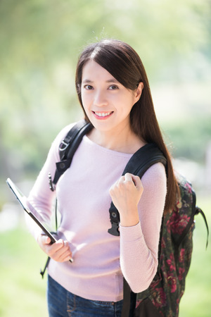 young woman student smile with digital tablet and show fist gesture. nature green background, asian beautyの写真素材