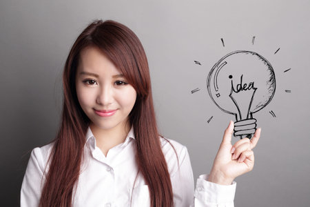 confident business woman hold light bulb isolated over gray background, asian beautyの写真素材