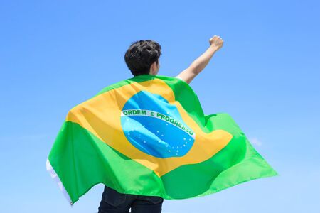Back view of a excited man holding a brazil flag with blue skyの写真素材