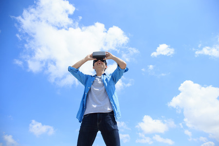 Smile happy man getting experience using VR-headset glasses of virtual reality with sky and cloud background, asian male