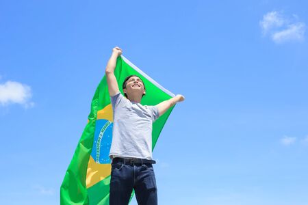 Excited man holding a brazil flag with blue skyの写真素材