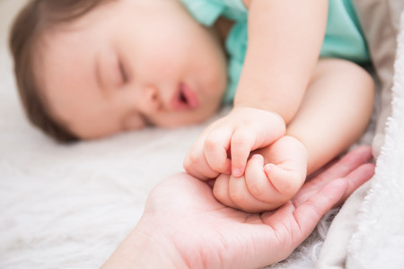 big hand hold cute baby fist and baby sleep on the white bed in bedroom, caucasianの写真素材