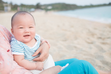 cute baby smile happily in adult arms in the beach, asian