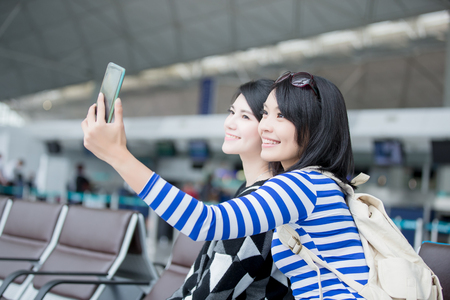 two beauty woman take smart phone and selfie in hong kong airport, asianの写真素材