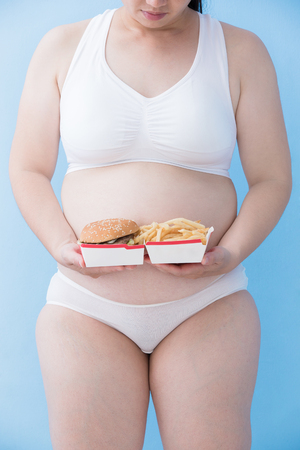 Fat overweight woman hold hamburger with blue background, asianの写真素材