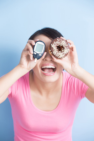 Woman holding a blood glucose meter and donut to prevention diabetes isolated on blue background, asianの写真素材