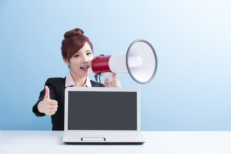 business woman take microphone shouting happily and show computer to you with isolated on blue background, asianの写真素材