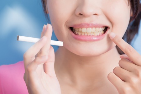 Woman holding cigarettes with yellow teeth isolated on blue background, asian