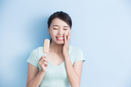 woman have sensitive teeth with ice isolatd on blue background, asian