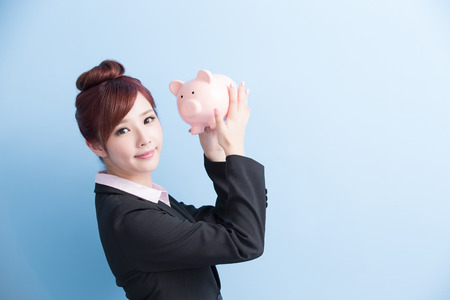 business woman take pink piggy bank and smile to you isolated on blue background, asianの写真素材