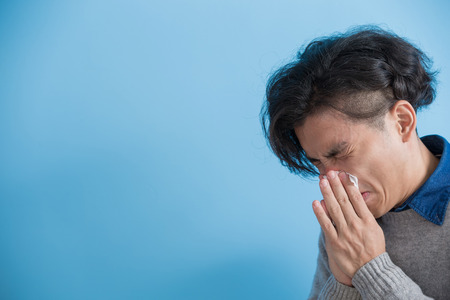 man is sick and sneezing with blue background, asianの写真素材