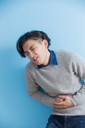 man feel stomach ache with isolated blue background, asianの写真素材