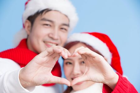 couple show heart gesture with merry christmas on the blue backgroundの写真素材