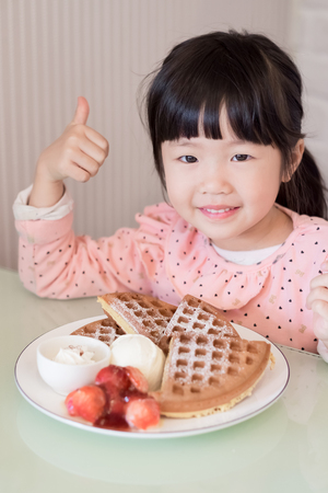 cute girl thumb up with strawberries wafflesの写真素材