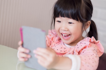 cute girl play phone and smile happilyの写真素材