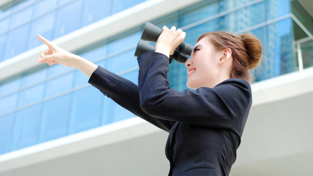 Business woman with binocular looking forward with office buildingの写真素材