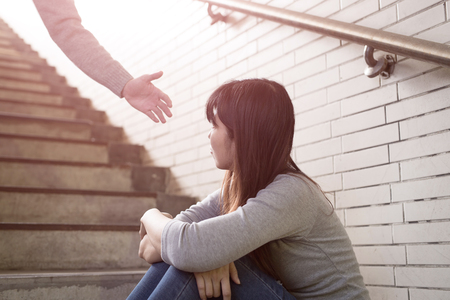 depressed woman sit in underground with a hand coming and offers helpの写真素材