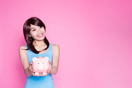 woman take piggy bank and look somewhere on the pink backgroundの写真素材