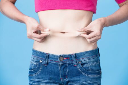woman pinch her belly on the blue backgroundの写真素材