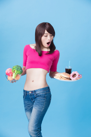 woman choose vegetable or junk food with body health concept on the blue backgroundの写真素材