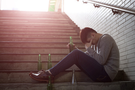Depressed man feel upset with alcoholism problem and sit in undergroundの写真素材