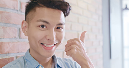 man look you and smile happily and show thumb up with brick wallの写真素材