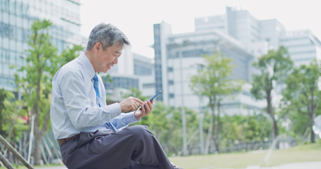 old businessman smile happily and use phoneの写真素材