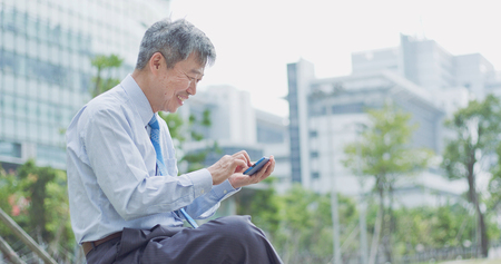 old businessman smile happily and use phoneの写真素材