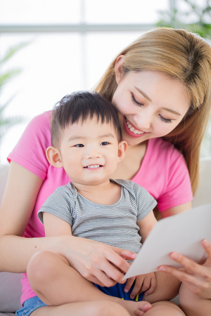 mom read book with son and sit on sofa at homeの写真素材