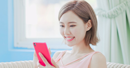 woman sit on sofa and use phone happily at homeの写真素材