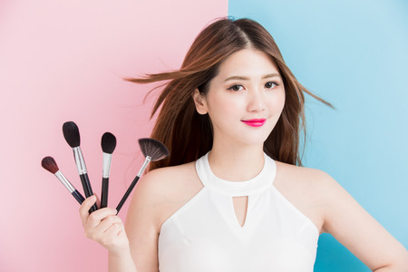 pretty girl take makeup brush in white dress isolated on a pink and blue backgroundの写真素材