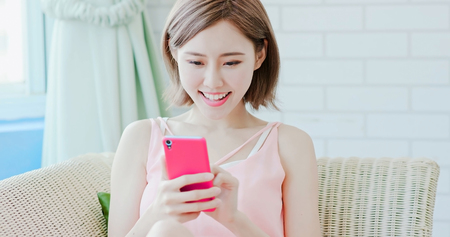 woman sit on sofa and use phone happily at homeの写真素材